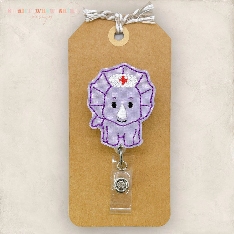 a brown paper tag with a purple embroidered nurse's hat and a clear plastic badge holder attached to it.