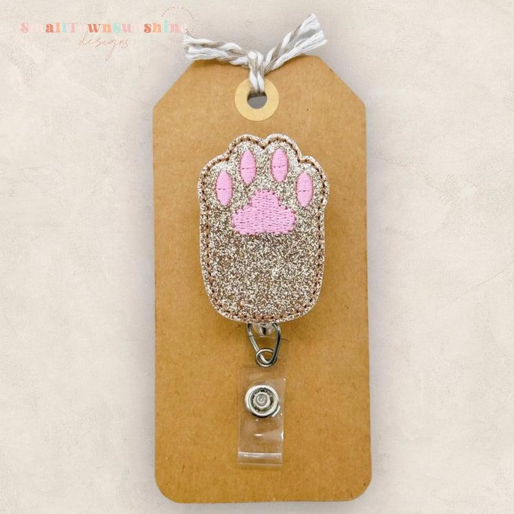 A brown paper tag with a glittery paw print charm attached to it.