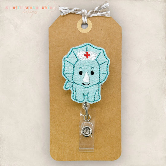 A handmade nurse badge with a blue triceratops design, attached to a brown paper tag.